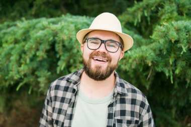 Laughing attractive man wearing hat over green tree background - emotion and vacation travel holidays