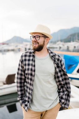 Yatı olan yat limanının yanında şapka ve gözlük takan yakışıklı bir adam. Deniz kenarı geçmişi olan gülen adam portresi..