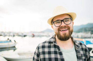 Handsome man wearing hat and glasses near marina with yachts. Portrait laughing man with sea port background with copy space