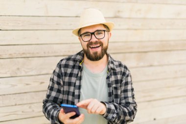 Gülümseyen erkek turist, yaz kenti boyunca ahşap duvarları aşarken akıllı telefon kullanıyor. Teknolojiler ve sosyal medya uygulaması.