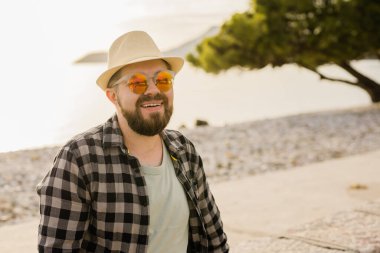 Handsome and confident. Outdoor portrait smiling man wearing hat and sunglasses on beach. Holidays travel and summer tourism