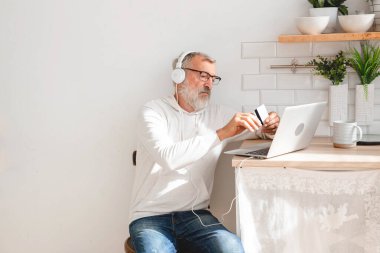 Üst düzey yaşlı adam dizüstü bilgisayarla online ödeme yapıyor. Gülümseyen yaşlı büyükbaba kredi kartıyla alışveriş yapıyor. Emeklinin elinde internet bankacılığı için banka kartı var