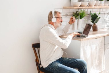 Üst düzey yaşlı adam dizüstü bilgisayarla online ödeme yapıyor. Gülümseyen yaşlı büyükbaba kredi kartıyla alışveriş yapıyor. Emeklinin elinde internet bankacılığı için banka kartı var