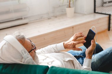 Son sınıf hipster 'ı cep telefonuyla mobil uygulama üzerinden müzik dinlerken kullanıyor. Yaşlı erkek video akıllı telefon izlerken yüz koruyucu maske takıyor.