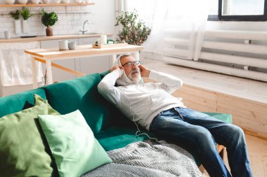 Son sınıf hipster 'ı cep telefonuyla mobil uygulama üzerinden müzik dinlerken kullanıyor. Yaşlı erkek video akıllı telefon izlerken yüz koruyucu maske takıyor.