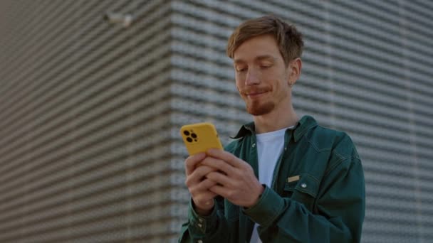 Hombre pelirrojo positivo usando el teléfono celular en la calle — Vídeos de Stock