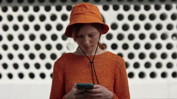 Roodharige meisje in oranje panama hoed met behulp van smartphone op straat — Stockvideo