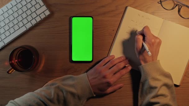 プランナーに書き、緑の画面でモバイルを使用して男 — ストック動画