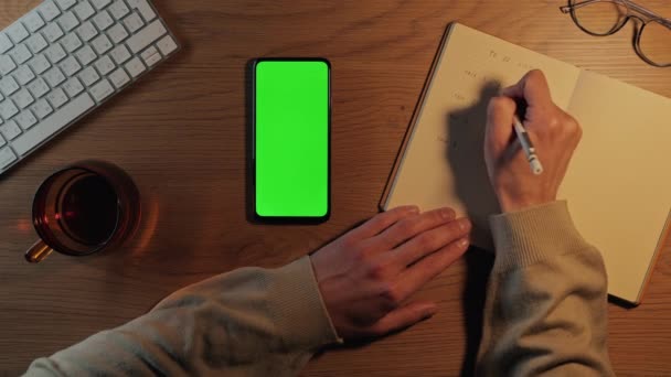 Liste yapmak için wirting yaparken yeşil ekranlı cep telefonu kullanan adam — Stok video