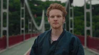 Kırmızı kıvırcık saçlı çekici erkek hippinin portresi dışarıda dururken kişisel cep telefonunu online iletişim için kullanıyor. Yakışıklı adam gülümsüyor ve kameraya bakıyor..