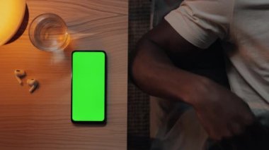 Yeşil ekranlı telefon yanında yatarken Afrikalı Amerikalı bir adam uyuyor.