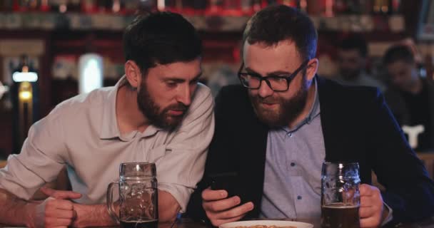 Dois velhos amigos com smartphone conversando no bar de cerveja à noite. Amigos rindo e discutir as notícias no pub de cerveja. — Vídeo de Stock