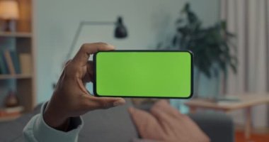 Afrika kökenli Amerikalı adam elinde yeşil ekranlı modern akıllı telefon tutuyor.