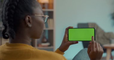 Kanepede oturan ve elinde yeşil ekran cep telefonu olan bir kadın.