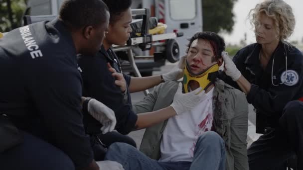 Многорасовая группа парамедиков, помогающих азиатскому мужчине на дороге — стоковое видео