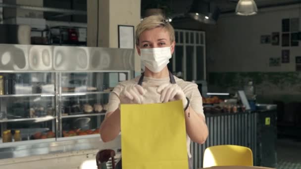 Официантка в маске и перчатках держит сумку с едой на вынос — стоковое видео