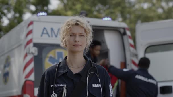 Paramédico femenino de pie en la calle con ambulancia detrás — Vídeos de Stock