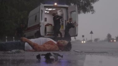 Sağlık ekibi, yağmurda yolda yatan adama yardım ediyor.