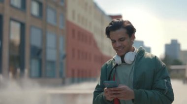 Boynunda kulaklık olan bir adam yürürken cep telefonu kullanıyor.