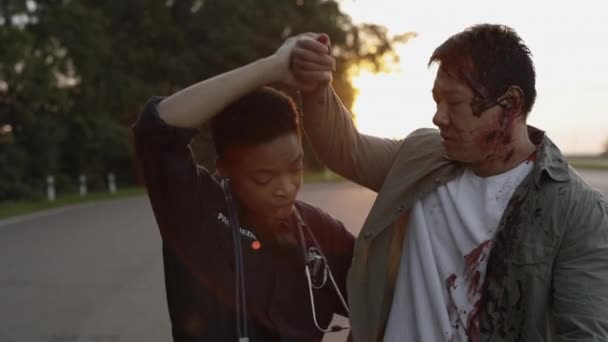 African american female paramedic helping injured asian man on road — Stock Video