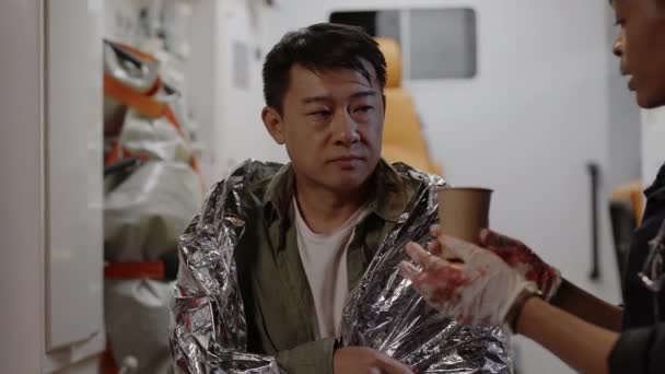 Doktor dává čaj asijskému muži, který sedí v sanitce — Stock video
