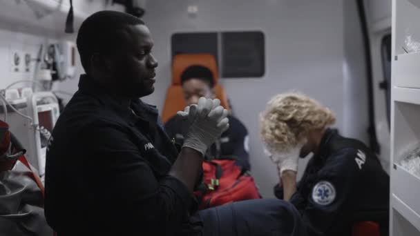 Nervösa afrikanska amerikanska ambulanssjukvårdare rider med multiraciala kollegor i ambulans till olycka på väg. Man läkare korsa sig själv, be till Gud och känna stress på jobbet. — Stockvideo