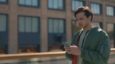 Şaşırmış bir adam dışarıda yürürken cep telefonuna bakıyor.