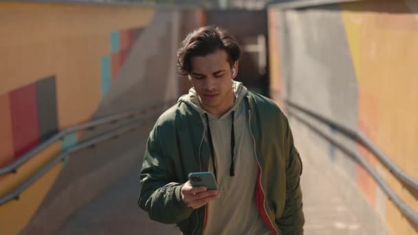 Веселый парень ходит по улице и пишет смс на смартфоне — стоковое видео