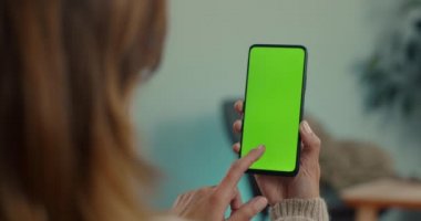 Kanepede oturan ve yeşil ekran cep telefonu kullanan kadın.