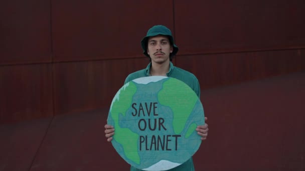 Молодой человек позирует на улице, спасая знамя нашей планеты — стоковое видео