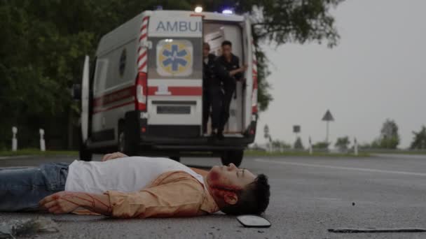 Multiracial paramedics helping injured asian man on road — Stock Video
