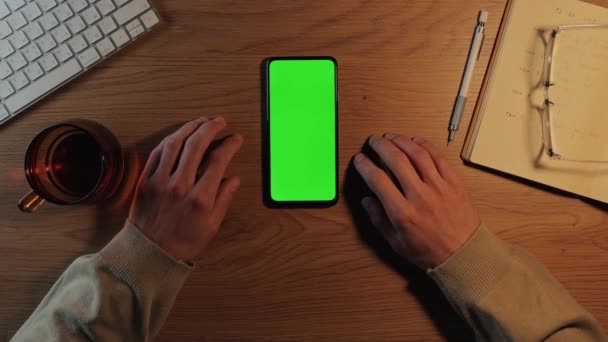 Man tikken op groen scherm van mobiele terwijl zitten aan het bureau — Stockvideo