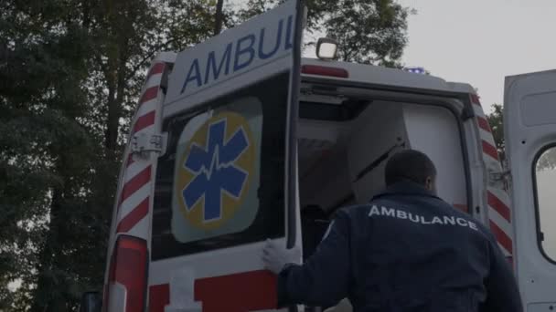 Africano paramédico americano com pressa fechando a porta do carro de ambulância — Vídeo de Stock