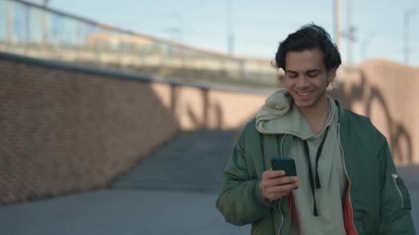 Uomo sorridente che utilizza lo smartphone mentre cammina per strada — Video Stock