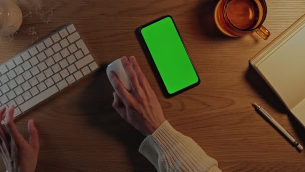 Mujer sentada en el escritorio con teclado y pantalla verde móvil — Vídeos de Stock