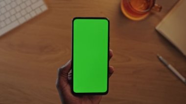 Siyah erkek elleri yeşil ekranlı dikey cep telefonunu tutuyor