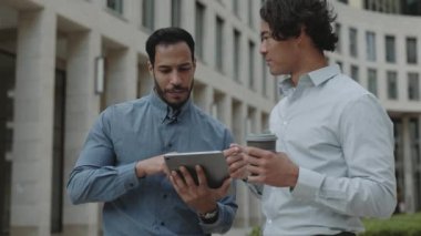 Açık havada tablet kullanan iki çok ırklı iş adamı.