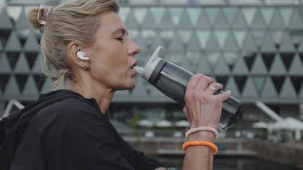 Mujer madura en los auriculares de agua potable después de ejecutar — Vídeos de Stock