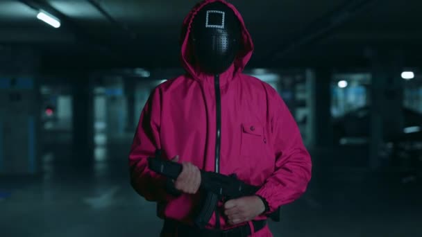 NEW YORK, NY, USA - November 10, 2021: Unrecognizable man in red overalls and black mask walking with gun in hands on underground parking. Armed guard from popular netflix serial of squid game. — Stock Video