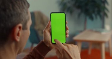 Orta yaşlı adam elinde yeşil ekranlı akıllı telefon tutuyor.