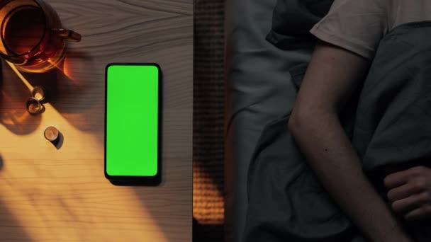 Мобільний з зеленим екраном лежить за столом, коли жінка спить — стокове відео