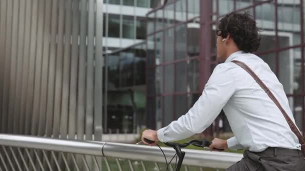 Бизнесмен в наушниках катается на велосипеде по городской улице — стоковое видео