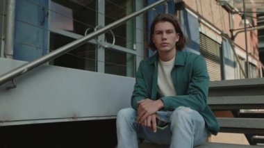 Dışarıda merdivenlerde oturan şık saç kesimli yakışıklı adam.