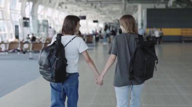 Mutlu lezbiyen çift el ele tutuşup havaalanında yürüyor.