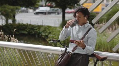 Asyalı işadamı kahve içiyor ve cep telefonu kullanıyor