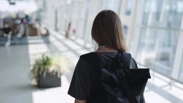 Achteraanzicht van een vrouw met rugzak die alleen op het vliegveld loopt — Stockvideo