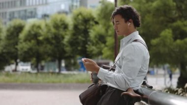 Cep telefonu kullanan ve kahve içen kulaklıklı bir Asyalı.