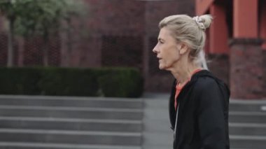 Olgun beyaz kadın şehir caddesinde koşudan sonra mola alıyor.