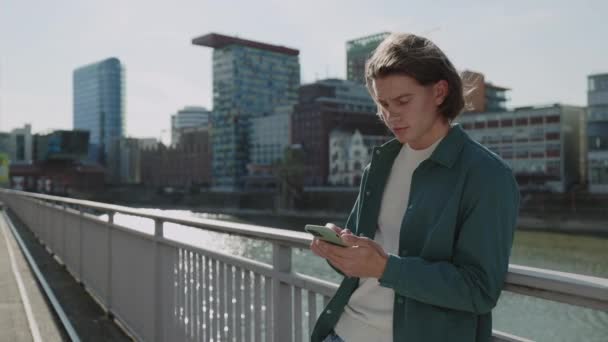 Νεαρός που χρησιμοποιεί σύγχρονο smartphone στέκεται στο δρόμο — Αρχείο Βίντεο