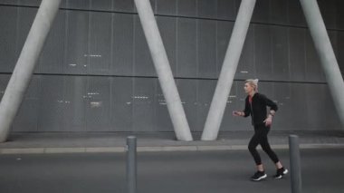 Şehir caddesinde koşan siyah spor elbiseli yaşlı kadın.